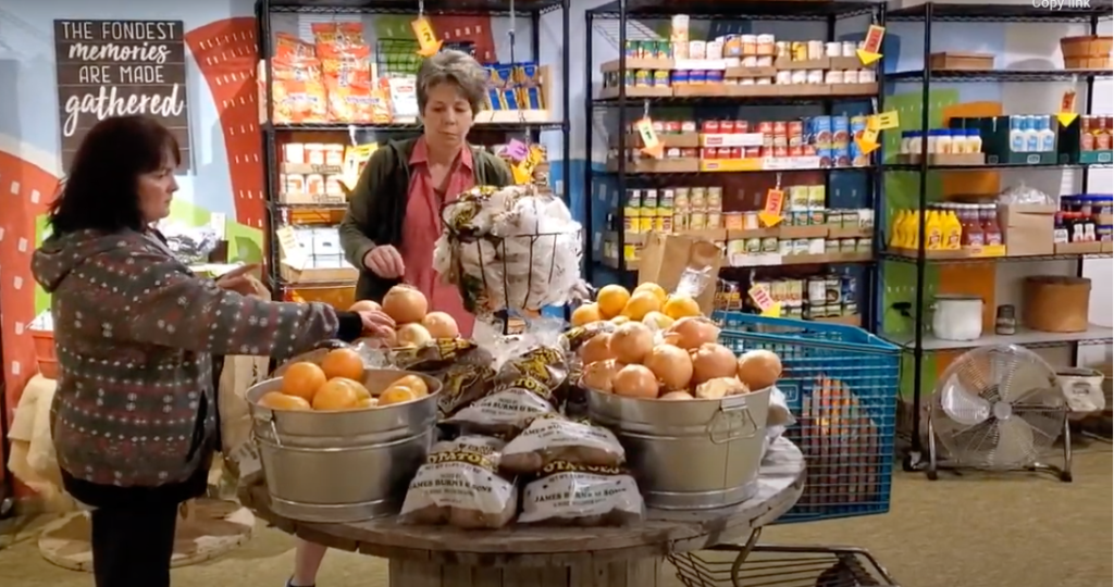 Two women shopping, selecting grapefruits from a table of produce.