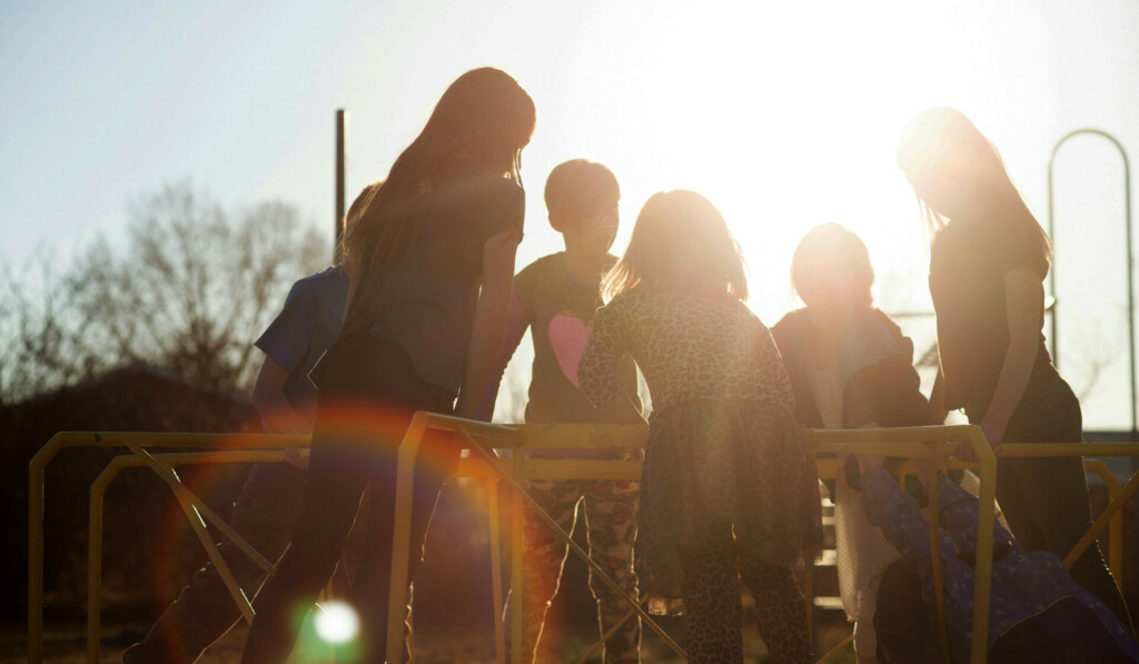 A group of kids playing on a merry-go-round at sunset.